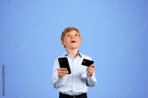 Boy with phone and credit card, happy portrait on empty blue background