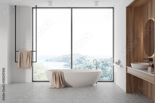 Light bathroom interior with sink and mirror, tub near panoramic window © ImageFlow