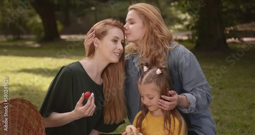 Young lgbtq couple with daughter enjoying a picnic