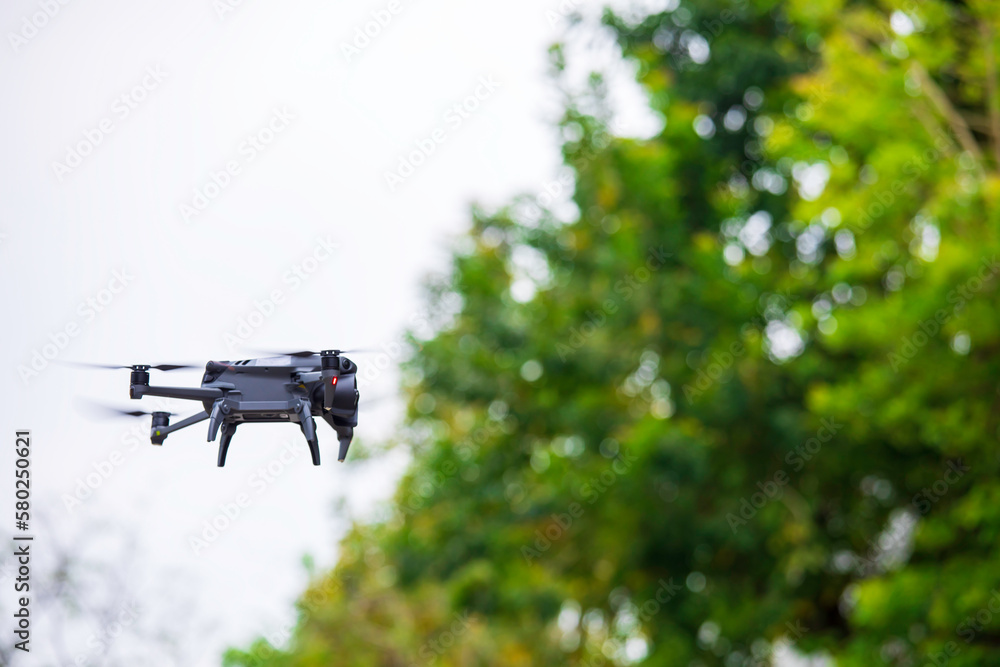 Modern drone flies in the forest. Dark drone in the air against Modern drone flies in the forest. Dark drone in the air against