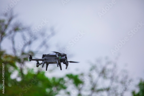 Modern drone flies in the forest. Dark drone in the air against