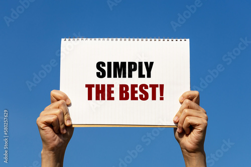 Simply the best text on notebook paper held by 2 hands with isolated blue sky background. This message can be used as business concept about making thing simple is the best