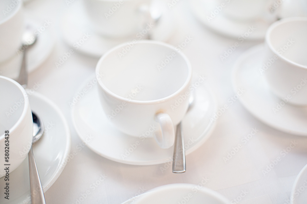 Many rows of white ceramic coffee or tea cups. Lines of coffee cups in front of conference room. White ceramic cups and saucers laid out on a buffet table at a catered event for serving a hot beverage