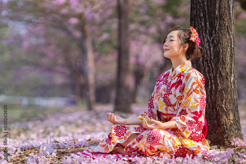 Japanese woman in kimono dress is doing meditation under sakura tree during cherry blossoming season for inner peace, mindfulness and zen practice Japanese woman in kimono dress is doing meditation under sakura tree during cherry blossoming season for inner peace, mindfulness and zen practice