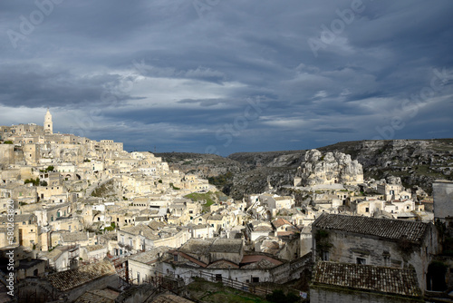 View the town of Matera (Unesco Heritage) and its famous "Sassi", ancient stone engraved dwellings, illuminated by sunbeams, dramatic sky clouds in Winter