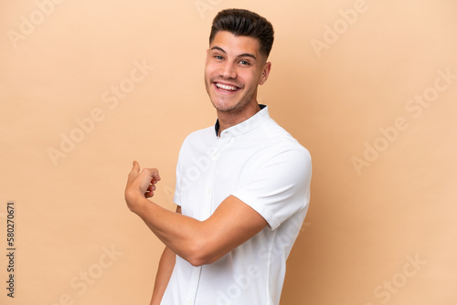 Young caucasian man isolated on beige background pointing back