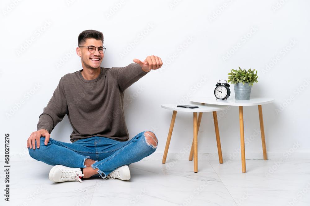 Young caucasian man sitting in his home isolated on white background giving a thumbs up gesture Young caucasian man sitting in his home isolated on white background giving a thumbs up gesture