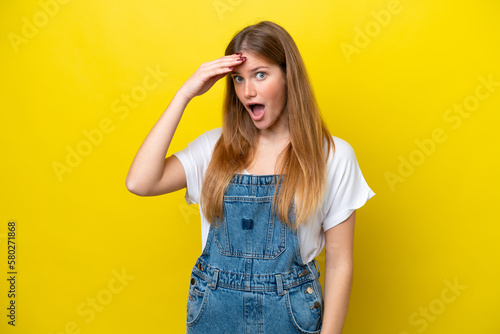 Young caucasian woman isolated on yellow background doing surprise gesture while looking to the side