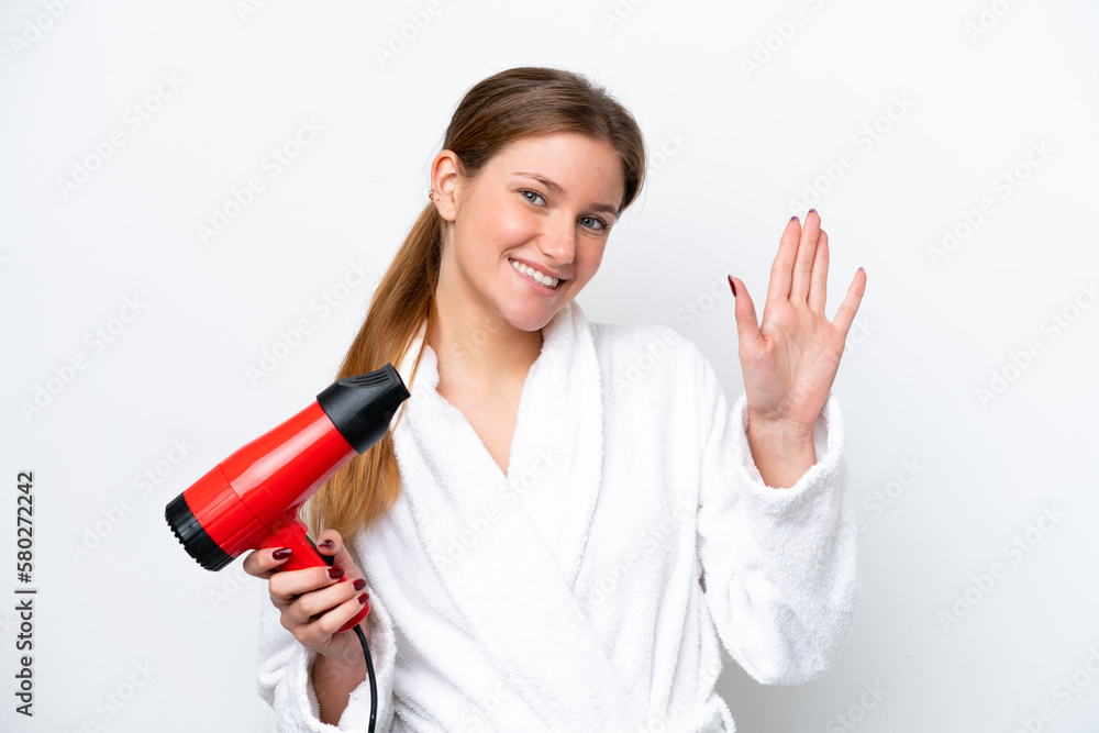 Young caucasian woman holding hairdryer isolated on white background saluting with hand with happy expression Young caucasian woman holding hairdryer isolated on white background saluting with hand with happy expression
