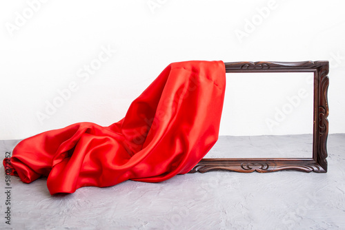 Red satin cloth unveiling a wooden brown frame, on cement table top photo