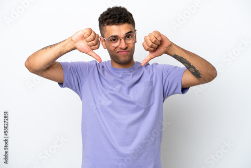 Young caucasian Brazilian man isolated on white background showing thumb down with two hands