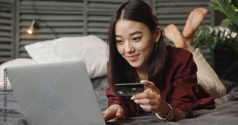 Smiling Asian woman look at laptop screen text message online on device. Happy young Japanese female use notebook browse wireless internet on gadget. Communication, technology,online shopping concept.