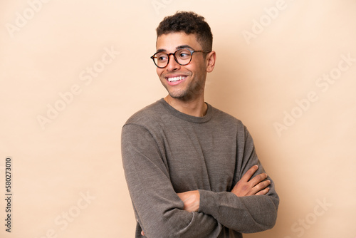 Young Brazilian man isolated on beige background looking to the side and smiling