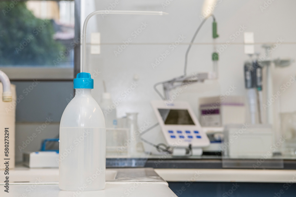 A splastic squirt bottle standing on the table in a laboratory with laboratory equiment in the background like a fume hotte and pH meter. A splastic squirt bottle standing on the table in a laboratory with laboratory equiment in the background like a fume hotte and pH meter.