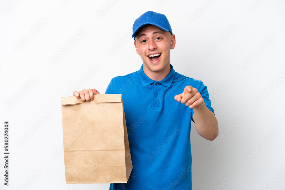 Young Brazilian man taking a bag of takeaway food isolated on white background surprised and pointing front Young Brazilian man taking a bag of takeaway food isolated on white background surprised and pointing front