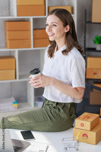 Concept of parcel delivery and selling online,Retailer holding coffee cup feel happy after check sales for the day on online store for pack parcel box and prepare to send the product to the customer