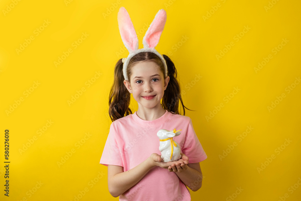 Beautiful teenage girl in a pink T-shirt and rabbit ears on a yellow background