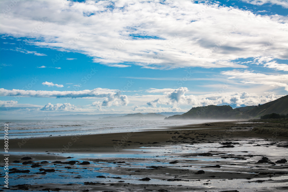 Mist rising over water and dark sand obscuring distant mountains. Makorori Beach, Gisborne, New Zealand