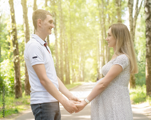 Young married happy couple walking in the park. Pregnant woman holding hands with her husband. Natural with no makeup. Couple holding hands on the pregnant belly. In love pregnant couple. Pregnancy.  © Нина Кулагина