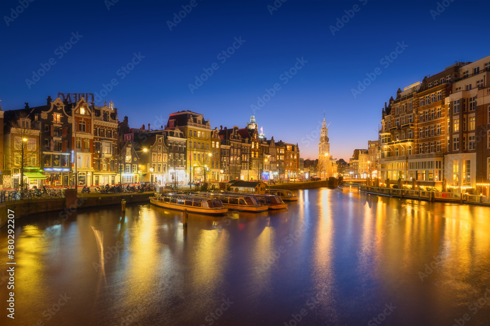 Amsterdam, Netherlands. Evening cityscape. Dark sky and city lights. Dutch canals. Reflections on the surface of the water. Photography for design and wallpaper.
