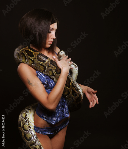 sexy brunette woman holding python over black background