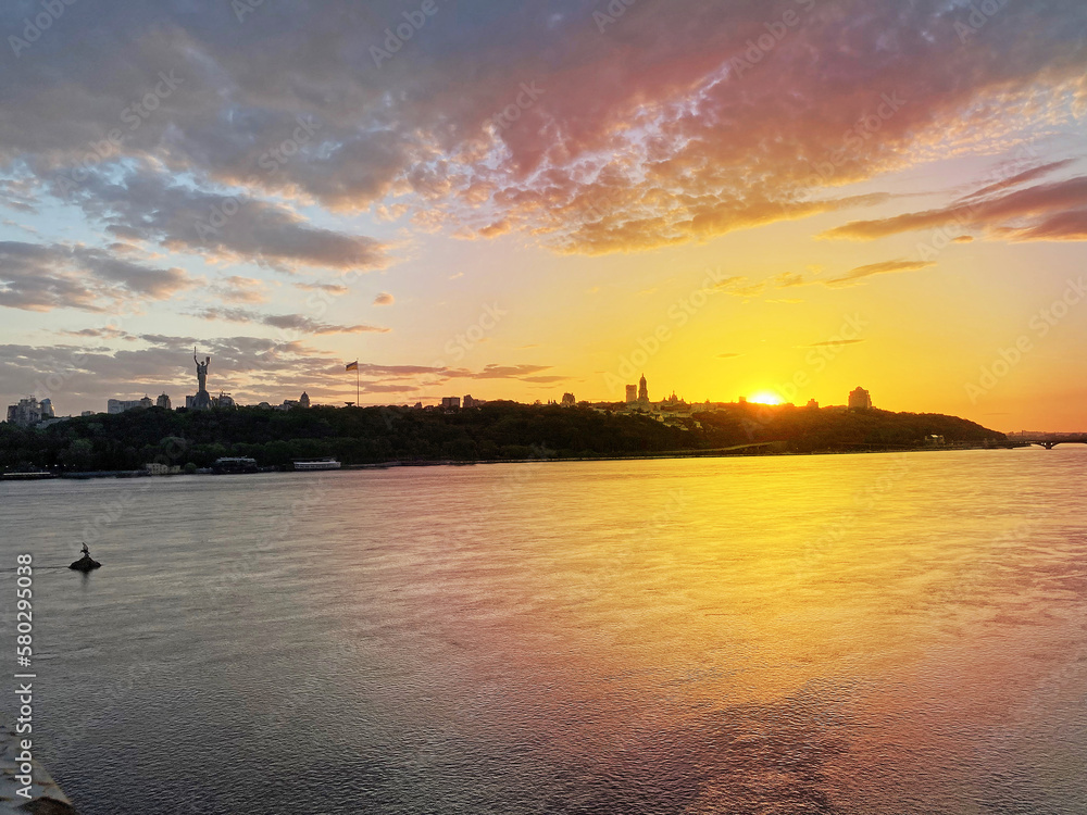 Dramatic colorful sunset over Dnipro river in Kiev, Ukraine. Historical sights of Ukraine. Beautiful scenic view of Kyiv. Sunset over the Dnieper River in Kiev. View of the river with waves