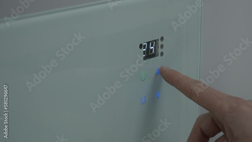 The male finger presses the touch button on the wall heater and adjusts the temperature in the room to 30. Heating system. close-up. High quality 4k footage