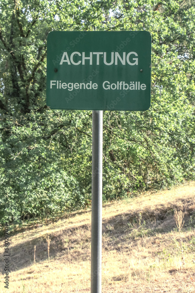 Grünes Schild mit Aufschrift: Achtung Fliegende Golfbälle