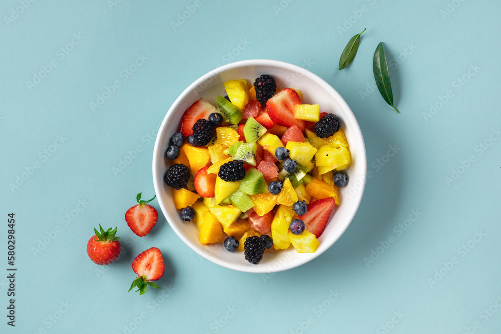 Bowl of healthy fresh summer mixed fruit salad on blue surface. Delicious and wholesome food background top view Bowl of healthy fresh summer mixed fruit salad on blue surface. Delicious and wholesome food background top view