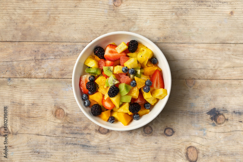 Bowl of healthy fresh summer mixed fruit salad on wooden table. Delicious and wholesome food background top view.