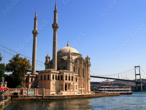 View of the beautiful Ortakoy Mosque with two minarets on the shores of the Bosphorus with the Bosphorus Bridge and a ship in the background in Istanbul, Turkey	