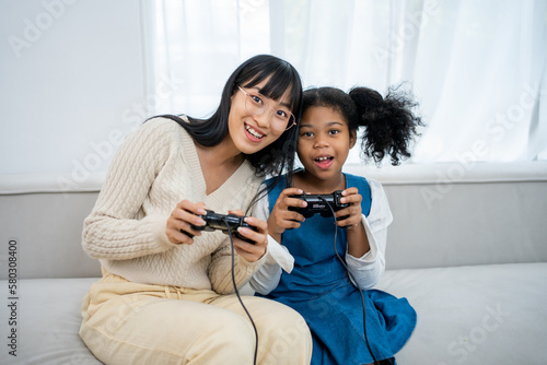 African american kid , baby sitter and cute little girl having fun together, playing video games, sitting on the couch. Leisure activities, babysitting concept.