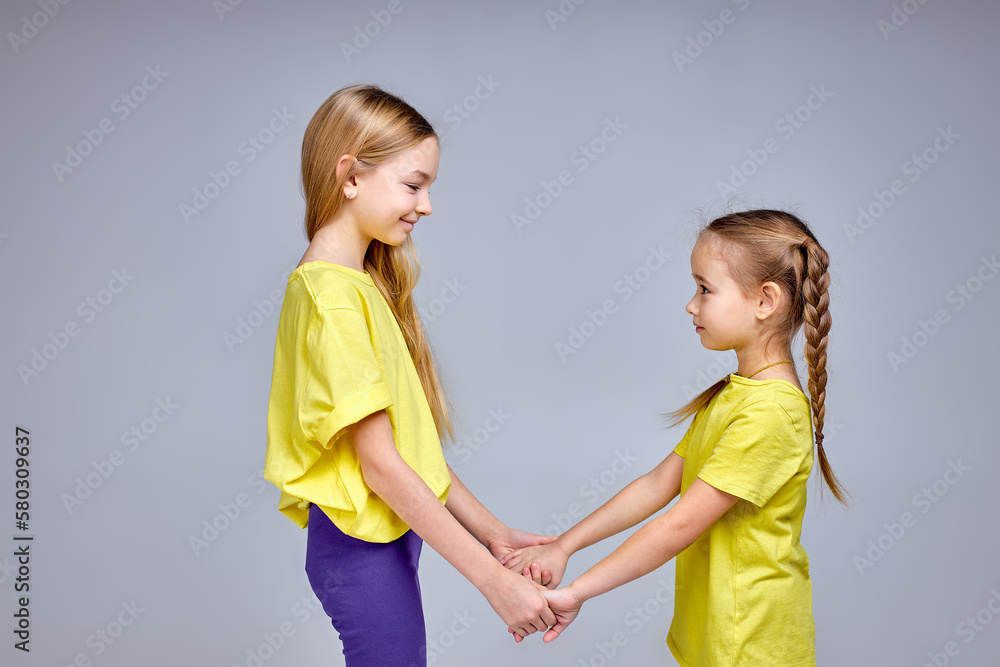 elder sister entertains her little one, two smiling awesome kids have fun at studio. making circle, holding hands, singing songs, dancing, isolated white background elder sister entertains her little one, two smiling awesome kids have fun at studio. making circle, holding hands, singing songs, dancing, isolated white background