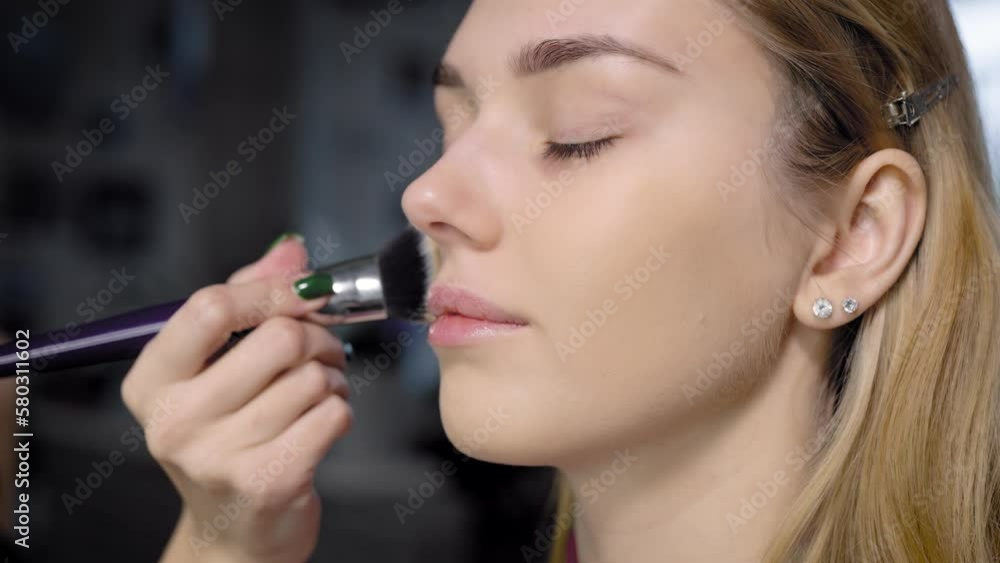 Close-up makeup artist applies foundation with a brush to the face of a young woman. Mua Close-up makeup artist applies foundation with a brush to the face of a young woman. Mua