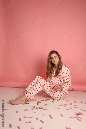 beautiful girl in heart print pajamas on a pink background. throw festive confetti. Pink pajamas with red hearts. clothes for sleep and home. Valentine's Day. beautiful blonde in pajamas