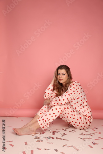 beautiful girl in heart print pajamas on a pink background. surprised look, Confetti. Pink pajamas with red hearts. clothes for sleep and home.