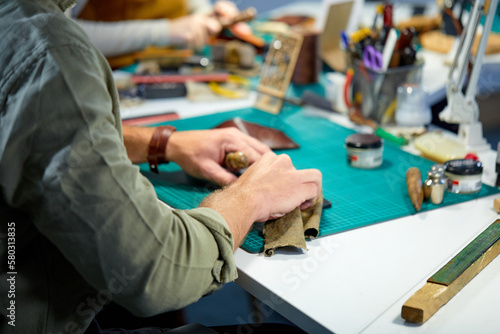 close up cropped shot, man smoothing the surface of leather product, focus on arms. tailor repairs old leather wallet. craftsman preparing pieces of leather for sewing