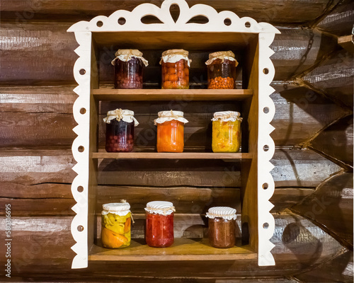 Canned compotes in large glass jars. on a wooden shelf against a log wall