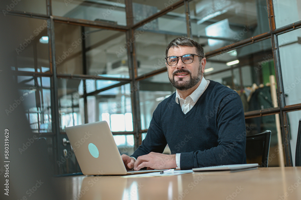 Happy man in glasses typing at laptop while sitting at the workplace Happy man in glasses typing at laptop while sitting at the workplace