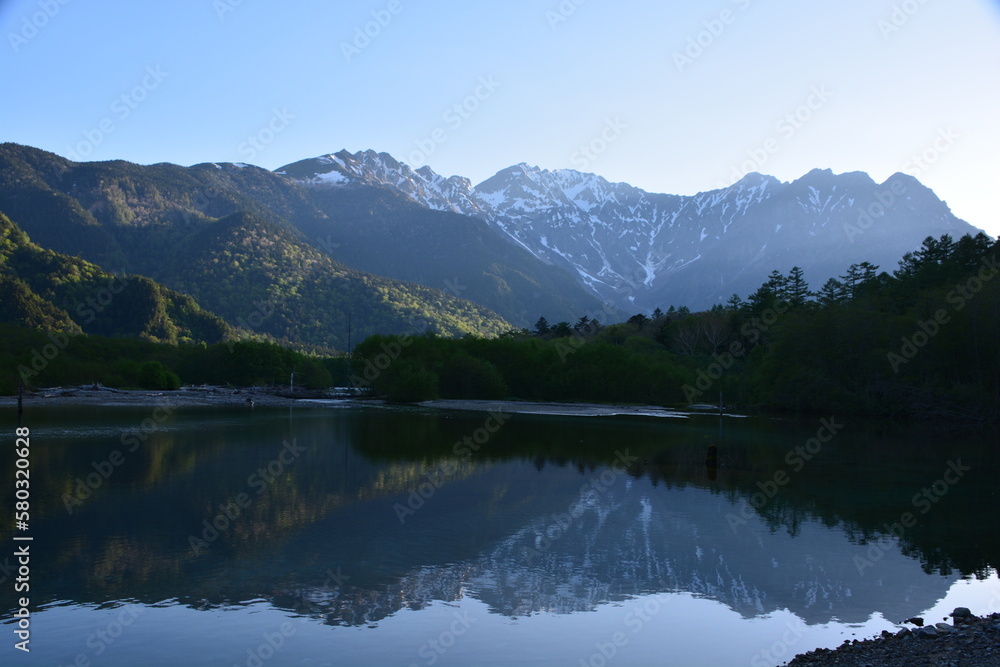 朝の大正池　初夏の日の出が新緑と残雪の穂高岳を照らす