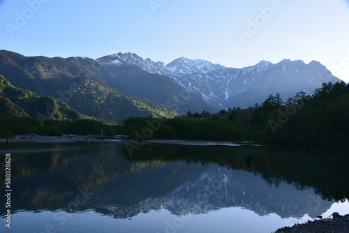 朝の大正池 初夏の日の出が新緑と残雪の穂高岳を照らす