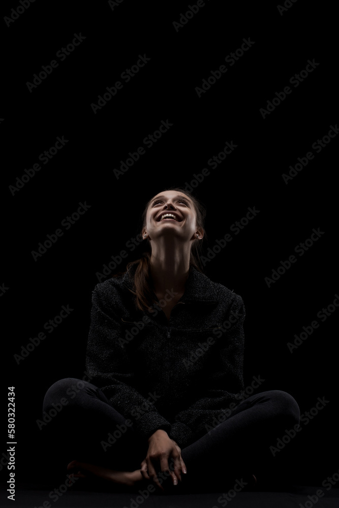 cute caucasian girl relaxing after yoga exercise against dark backgroung. side lit looking up and smiling..