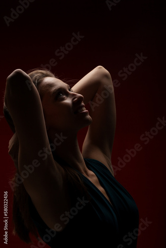 Cute girl against dark red background. Brunette lady wearing fancy shirt with hands up looking up.