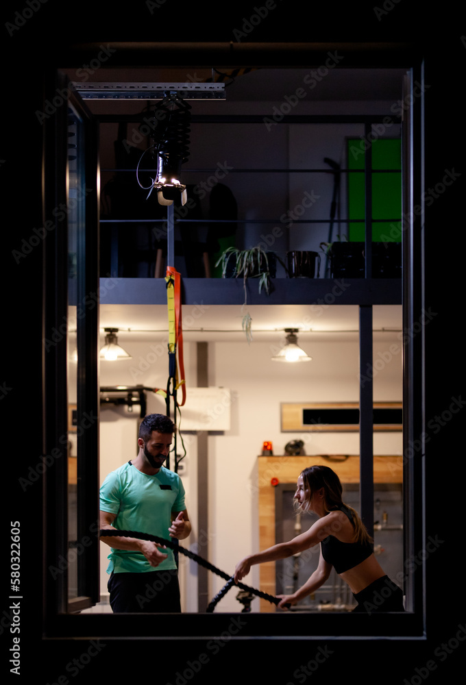 Fit girl with exercising with ropes with a male fitness instructor in a fitness studio. View from outside the window. Fit girl with exercising with ropes with a male fitness instructor in a fitness studio. View from outside the window.