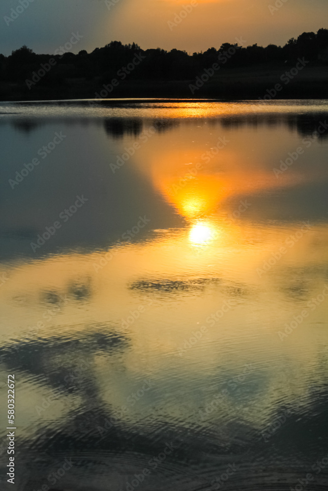 Beautiful sunset. The setting golden sun is reflected in the water surface on the lake. Vertical Beautiful sunset. The setting golden sun is reflected in the water surface on the lake. Vertical