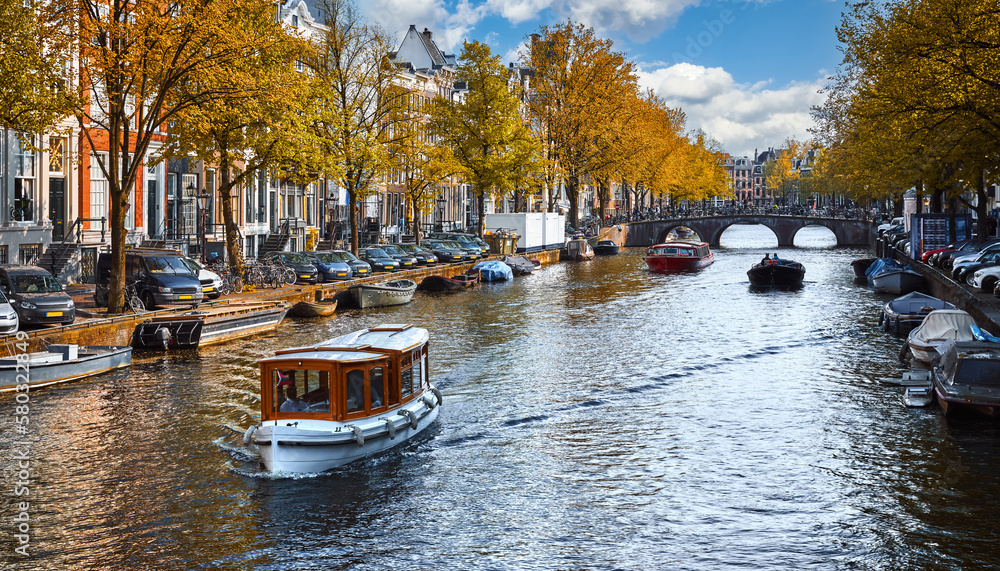 Channel in Amsterdam Netherlands Holland houses under river Amstel. Landmark old european city utumn landscape with sunshine. Pleasure boats tourists on the water