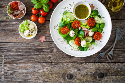 Fresh salad - prosciutto di Parma, mozzarella, cucumber, tomatoes and leafy vegetables on wooden table 