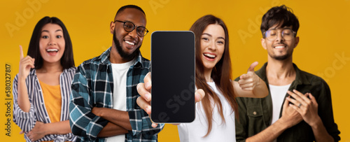 Happy millennial asian, black and arab guys and women point finger at phone with blank screen make gratitude gesture