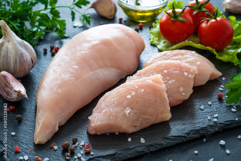 Fresh raw chicken fillet on cutting board with spices on black background
Fresh raw chicken fillet on cutting board with spices on black background