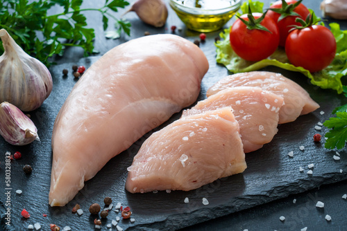 Fresh raw chicken fillet on cutting board with spices on black background 